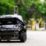 Ťažko poškodené čierne auto po dopravnej nehode zaparkované na okraji cesty.