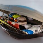 Otvorený strešný box plný športového vybavenia vrátane lyží, lyžiarok, prilieb a okuliarov.